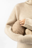 Modell im beigen Rippstrick-Rollkragenpullover hält Garnknäuel, Detailansicht zu statischer Aufladung bei Kaschmir