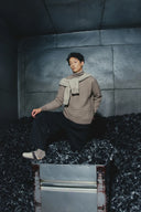 Modell in beigem Strickpullover mit Schal aus der Pre-Fall 2025 Kaschmir Kollektion, sitzend
