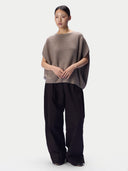 Model trägt taupefarbenes Oversize-Oberteil zu dunkler weiter Hose, Ganzkörperansicht