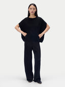 Model trägt schwarzes ärmelloses Strickoberteil zu weiter Hose, Ganzkörperansicht von vorn