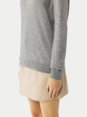 Detailansicht am Model: hellgrauer Pullover mit Rippensaum und Ärmelbündchen zum beigen Rock