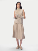 Model trägt das ärmellose Oberteil in natural beige mit plissiertem Rock und Armstulpen, Vorderansicht