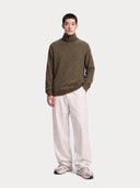 Modell trägt den olivfarbenen Rollkragenpullover zu weiter weißer Hose, Ganzkörperansicht von vorne