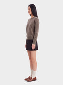 Model trägt den Pullover in Taupe in der Seitenansicht zu schwarzem Minirock und Loafern