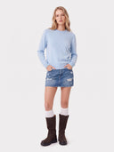 Model trägt den Kaschmirpullover in Soft Blue zu Jeans-Minirock und braunen Stiefeln, Ganzkörperansicht von vorne