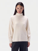 Weißer Kaschmir Rollkragenpullover im Linksstrick, weit geschnitten, von vorne an einem Model mit dunkler Hose
