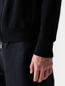 Detail von Ärmelbündchen, Saumrippe und Tasche der schwarzen Strickjacke am Model