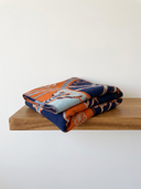 Gefaltet auf einem Holzregal, sichtbare Musterkanten in Orange, Blau und Soft Blue