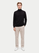 Modell trägt schwarzen Rollkragenpullover mit beiger Hose, Ganzkörperansicht von vorn
