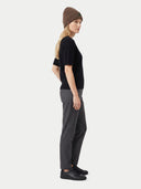 Seitenansicht des Models mit brauner Strickmütze, schwarzem Oberteil und grauer Hose