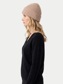 Seitenansicht der beigen Rippmütze am Modell, kombiniert mit schwarzem V-Ausschnitt-Pullover