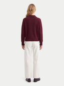 Rückansicht am Model: weinroter Kaschmir-Polopullover zu cremeweißer weiter Hose
