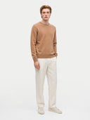 Modell trägt den Pullover in Warm Brown zu weißer Hose, Ganzkörperansicht von vorn