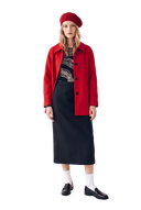 Frau in einer roten Kaschmir-Meltonjacke über einem schwarzen Pullover mit Seilknoten-Print, schwarzer Kaschmir-Rock, weiße Socken, schwarze Loafer und rote Strick-Beret