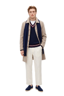 Mann in einem taupefarbenen Einreiher-Mantel aus Kaschmir über einem marineblauen Cricket-Pullover mit Zopfmuster, mit marineblauem Fransenschal, cremefarbener Hose und marineblauen Loafern