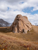 Granitfelsen auf herbstlichem Grasland vor schneebedeckten Bergen