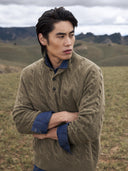 Mann in olivfarbenem Kaschmir-Polopullover mit Zopfmuster über einem Jeanshemd in der Steppe