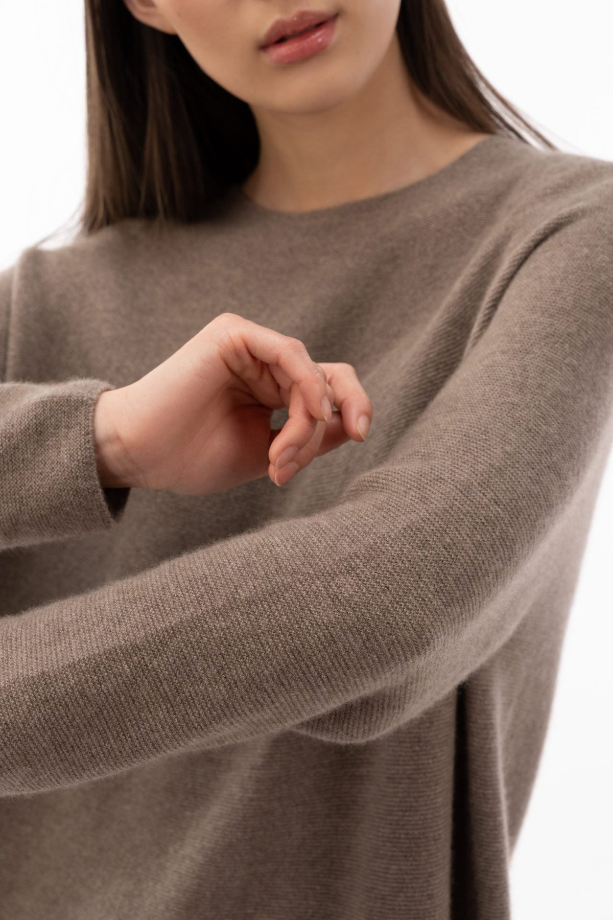 Nahaufnahme eines taupefarbenen Kaschmirpullovers mit verschränkten Armen, die durchgehende Strickstruktur ist zu sehen