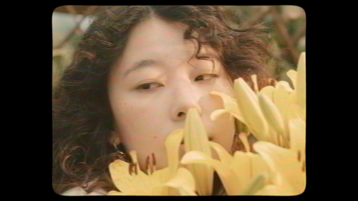 Frau mit dunklen Locken hinter gelben Lilien, Standbild aus dem Kampagnenfilm